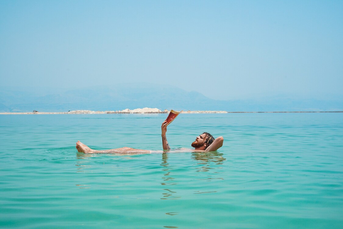 Baigneur lisant un livre allongé dans l'eau.